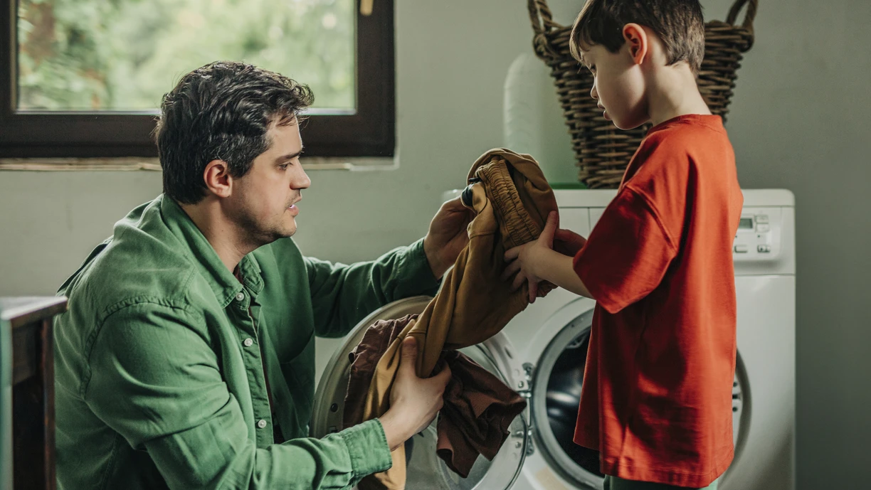 Father and son removing clothes from washing machine at home