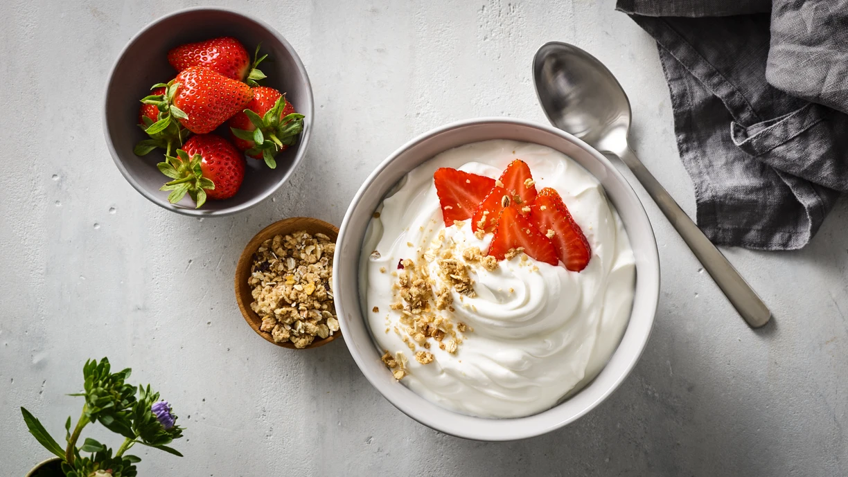 A bowl of plain, spoonable yogurt sprinkled with chopped strawberries and granola. 