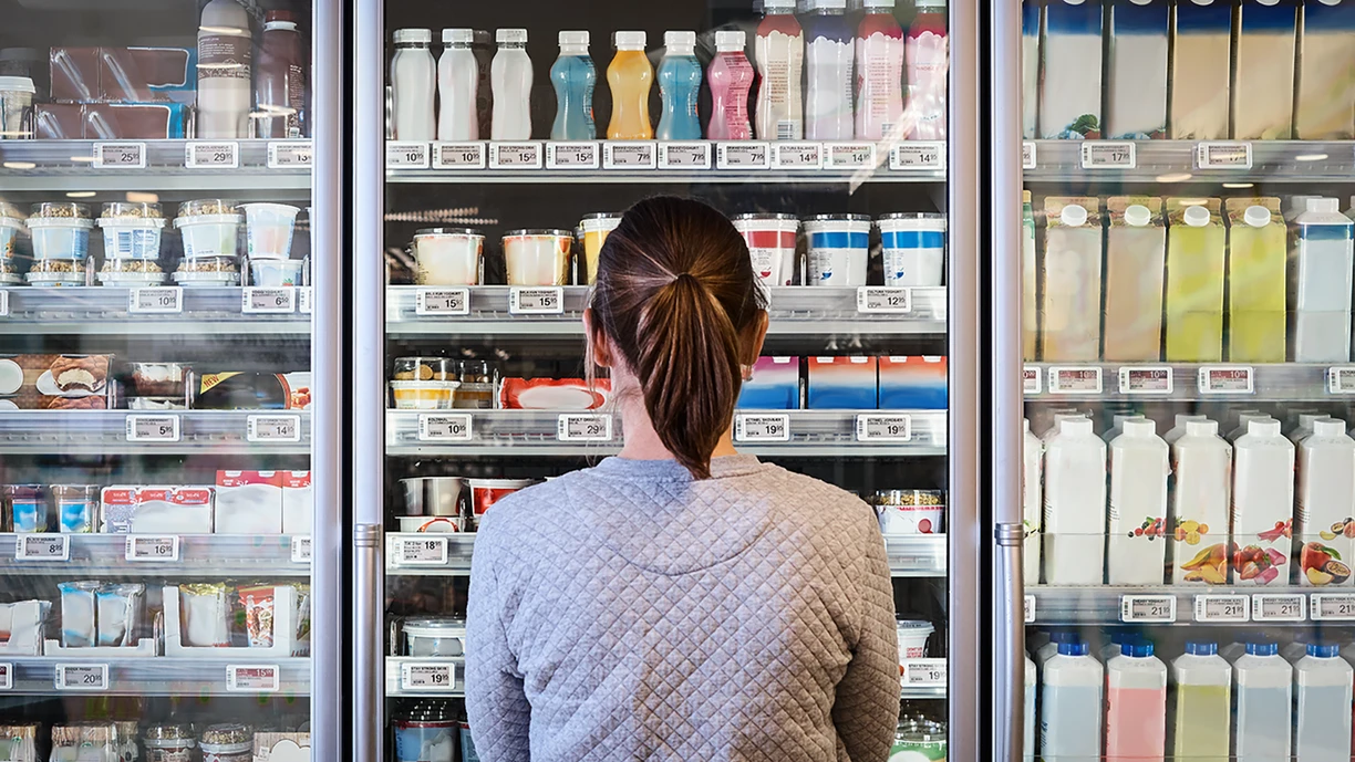 A woman in the supermarket dairy aisle, standing in front of a fridge containing a range of drinkable and spoonable yogurts  A woman in the supermarket dairy aisle, standing in front of a fridge containing a range of drinkable and spoonable yogurts  