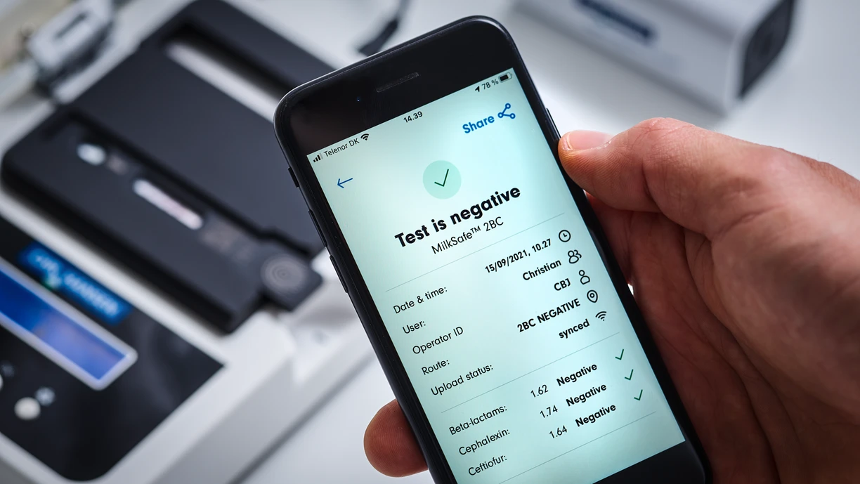 A person holding a smartphone showing test results, with lab equipment in the background