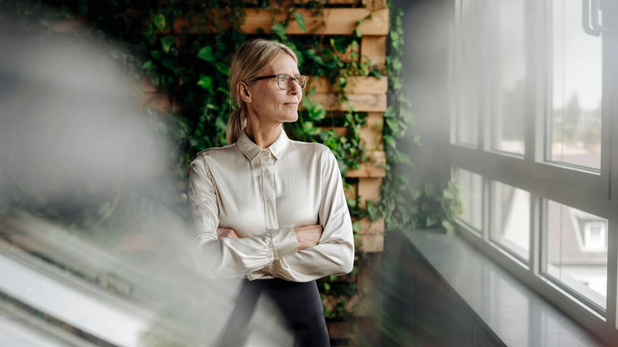 A woman gazing out the window while leaning against a wall made of timber and plants,  