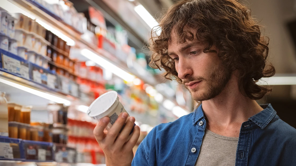 A young man looking at a spoonable yoghurt label in the dairy aisle of a supermarket 