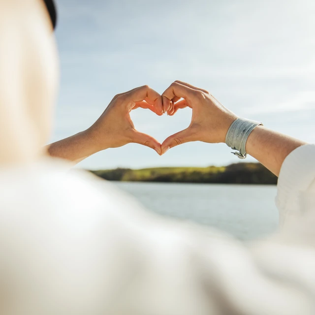 Woman gesturing heart shape in front of sky
