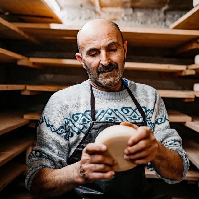 A cheesemaker in a ripening cave examining a wheel of comte for ripeness
