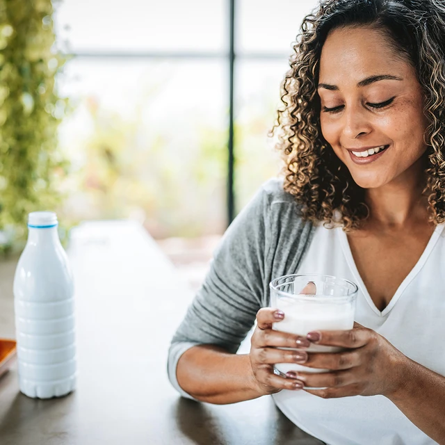 A woman sitting at her kitchen counter drinking a glass of milk