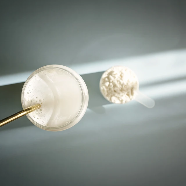 Top-down view of a glass of milk with a gold-colored straw, next to a scoop filled with powder. Related to milk adulteration and its detection