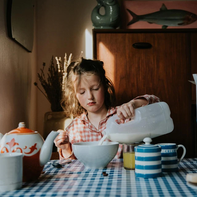 Child pouring milk into a bowl at a breakfast table