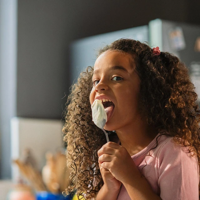 Girl licking spoon of yogurt
