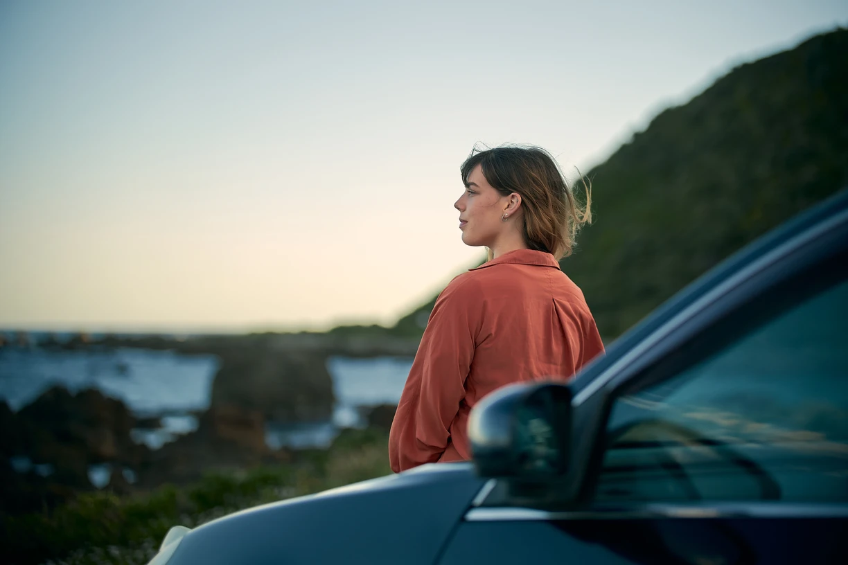 Woman standing beside car looking into the horizon