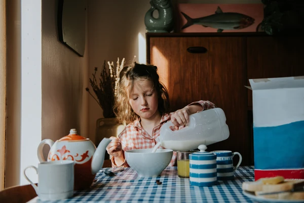 Girl pouring milk into bowl with cereal
