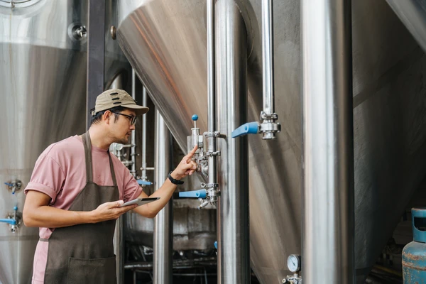 A brewer is checking the pressure gauge in his craft beer brewery at warehouse