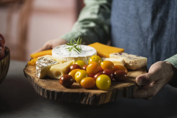 A man with a jeans apron with a cheese and tomatoes board