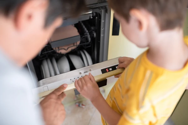 Little boy helping his father with dishwasher at home.