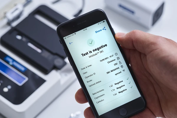MilkSafe™ test results showing on a mobile phone screen with the MilkSafe™ test kit visible in the background