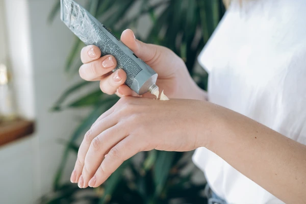 Woman with nude pink manicure squeezing cream on hand's skin to moisturize it