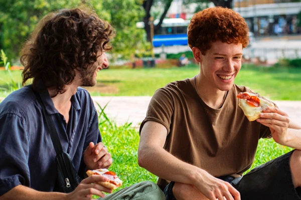 Two men eating pizza outside 