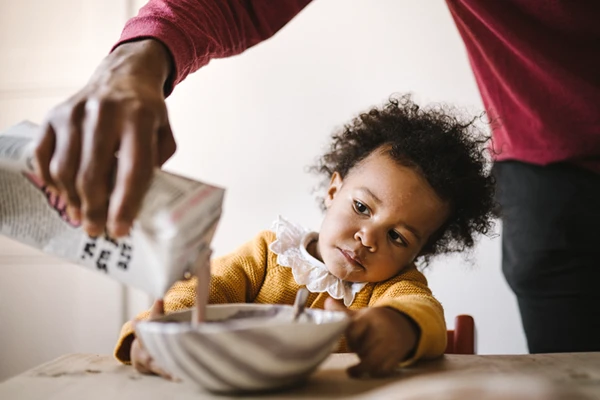 A little kid looking at her dad pouring yogurt