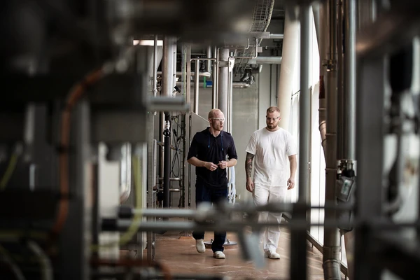 Two workers in a dairy walking through large-scale machinery while talking together 