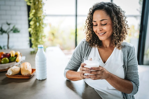 Woman with curly hair holding a glass of milk at a kitchen counter