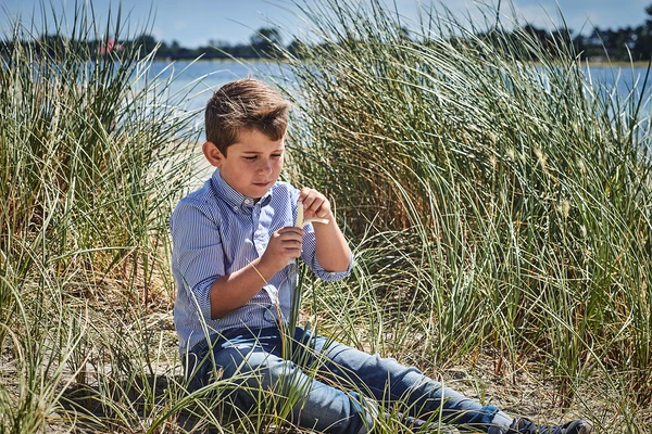 A little boy sitting on a beach eating string cheese  