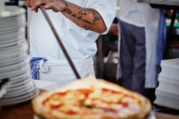 Chef in a pizza restaurant sliding a freshly baked pizza off a pizza peel 
