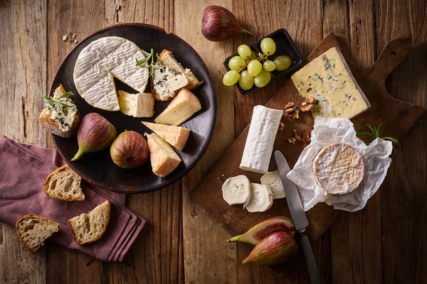 A range of soft cheeses on a wooden board, placed on a wooden table, with grapes, figs, bread and rosemary v