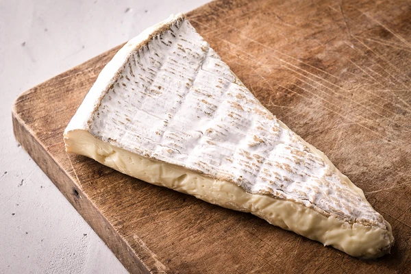 Wedge of soft, creamy cheese with a white rind on a wooden board. 