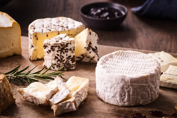 Assorted soft cheeses on a wooden board with herbs and jam—arranged to improve cheese flavor. 