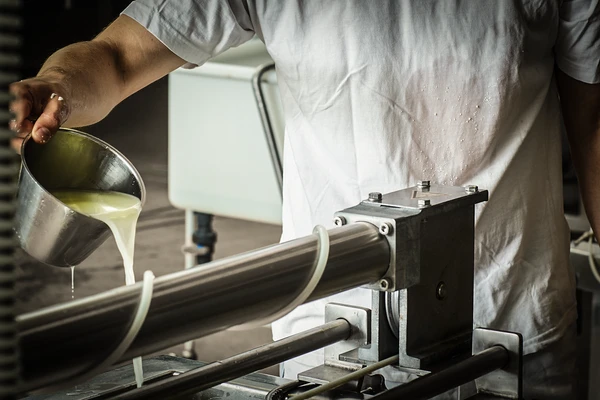 Worker in white t-shirt pouring liquid from a metal container into industrial food processing