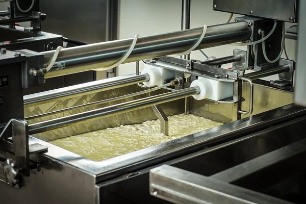 Stainless steel cheese-making machine processing cheese in a large industrial vat. Used in modern dairy production. 