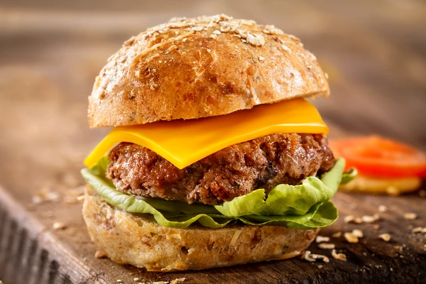 Close-up of a hamburger with a slice of melted cheddar cheese, lettuce, and a beef patty. 