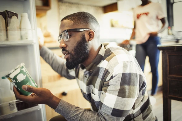erson kneeling in front of open fridge holding a yogurt container, possibly checking for shelf-life. 