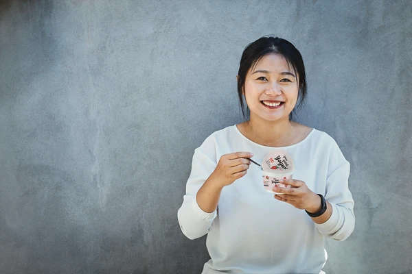 A young woman eating from an open pot of spoonable strawberry yogurt 