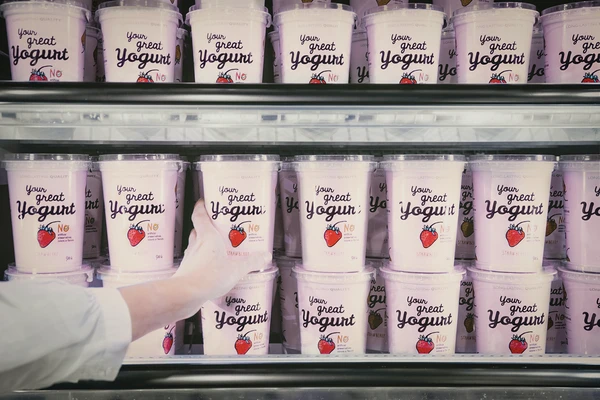 A hand reaching for a pot of strawberry yogurt in the dairy aisle of a supermarket 