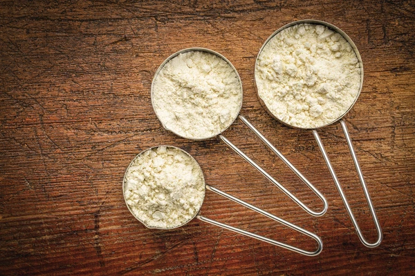 Three metal scoops of varying sizes filled with whey powder 