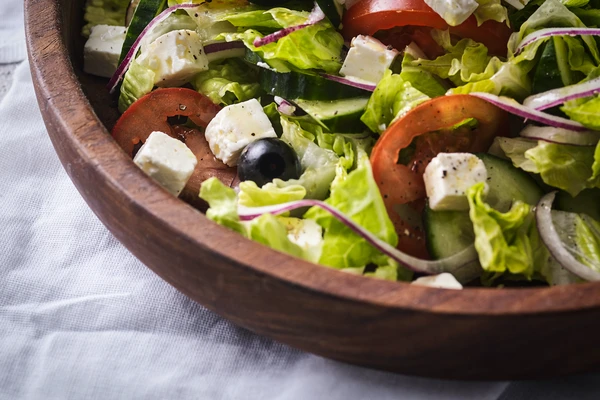 Wooden bowl filled with a fresh salad of chopped lettuce, tomatoes, cucumbers, red onions, black olivesWooden bowl filled with a fresh salad of chopped lettuce, tomatoes, cucumbers, red onions, black olives