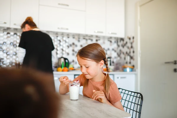 Young girl child has breakfast as her mom tidies up