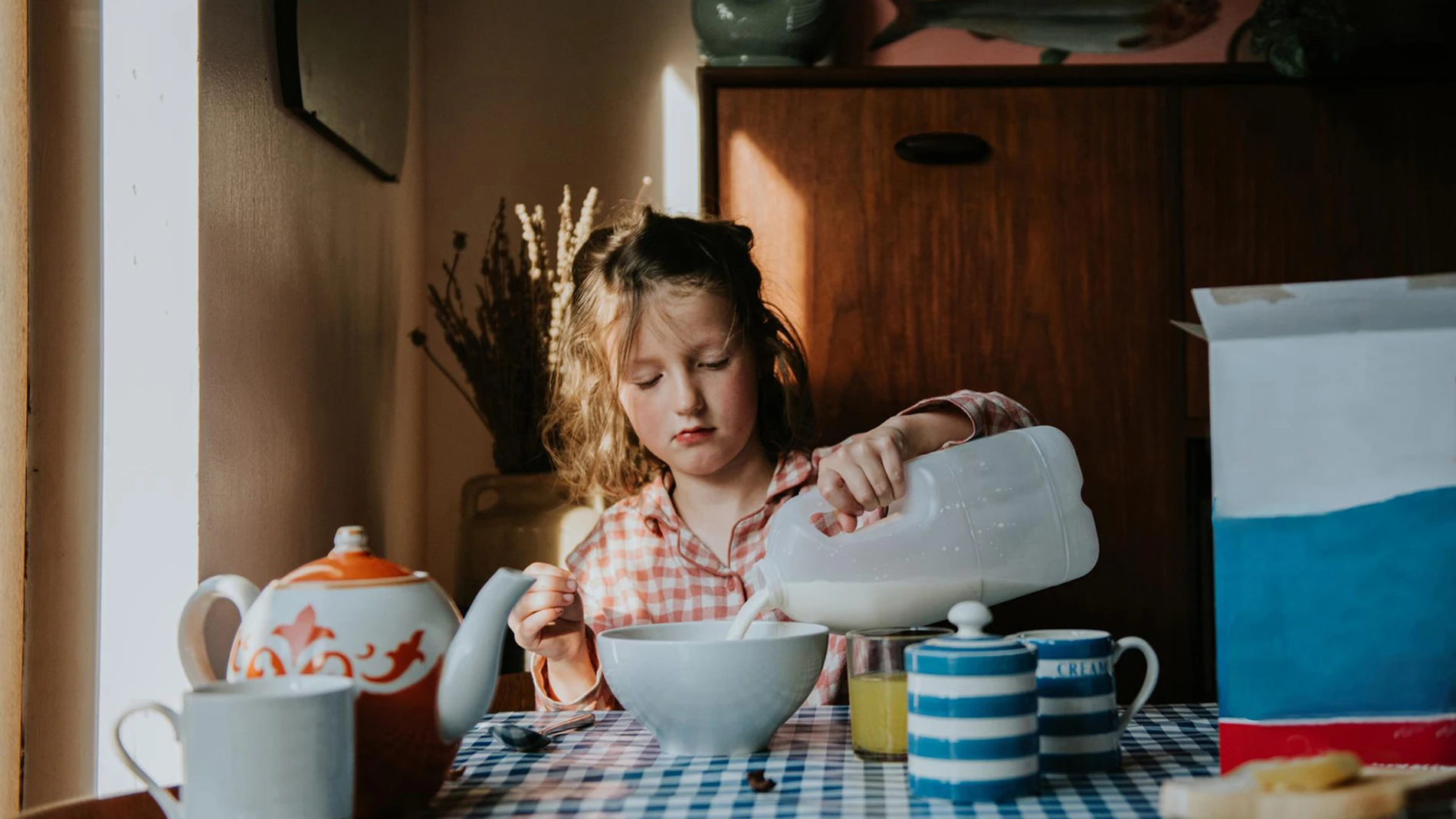 Child pouring milk into a bowl at a breakfast table