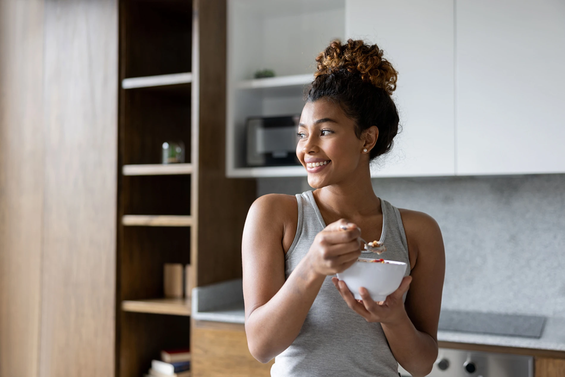 Woman at home eating a bowl of cereal with milk for breakfast and smiling