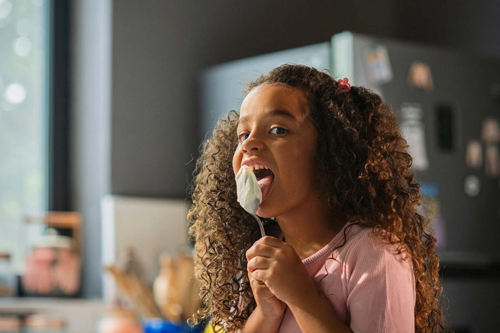 Little girl eating yogurt with a large spoon, and licking the spoon