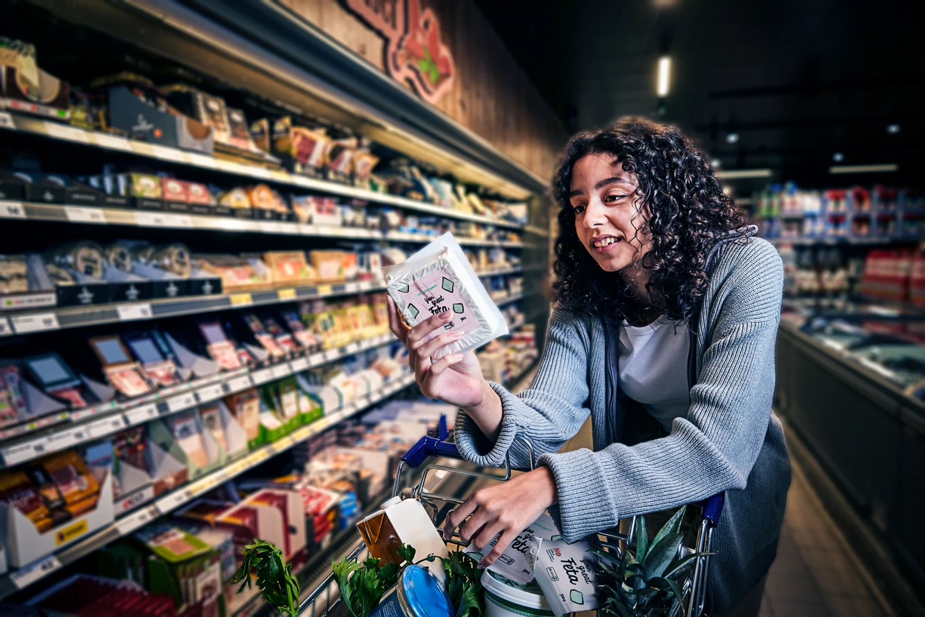 Woman with curly hair examines a package of feta cheese while shopping in a grocery store
