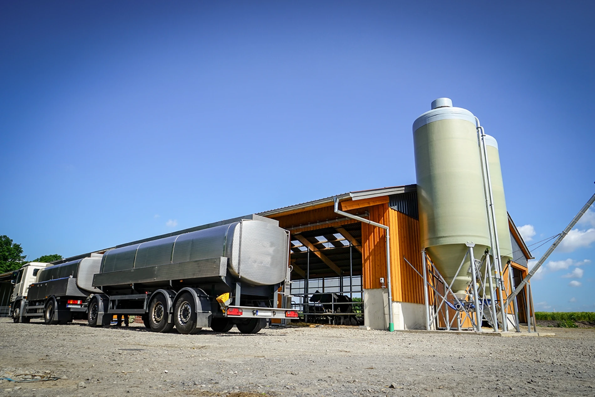 Tanker truck parked by a farm building with silo