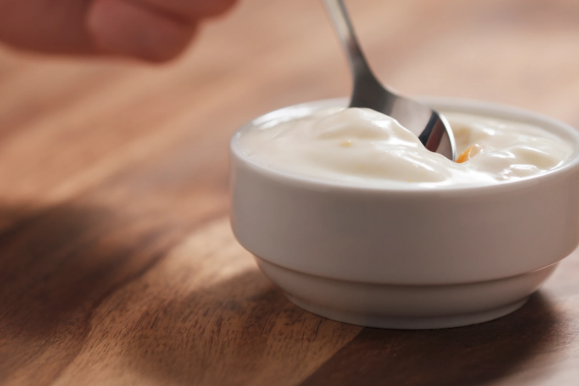 Young female hand eating peach yogurt with spoon.png