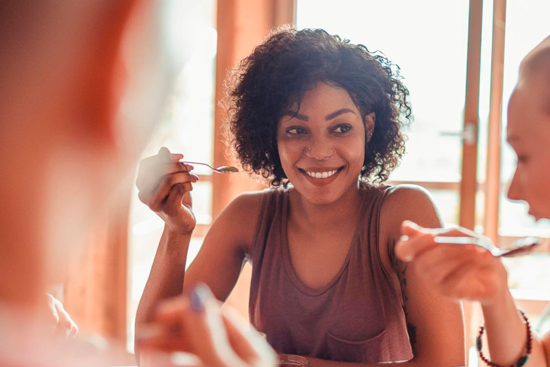 Young female hand eating peach yogurt with spoon.png